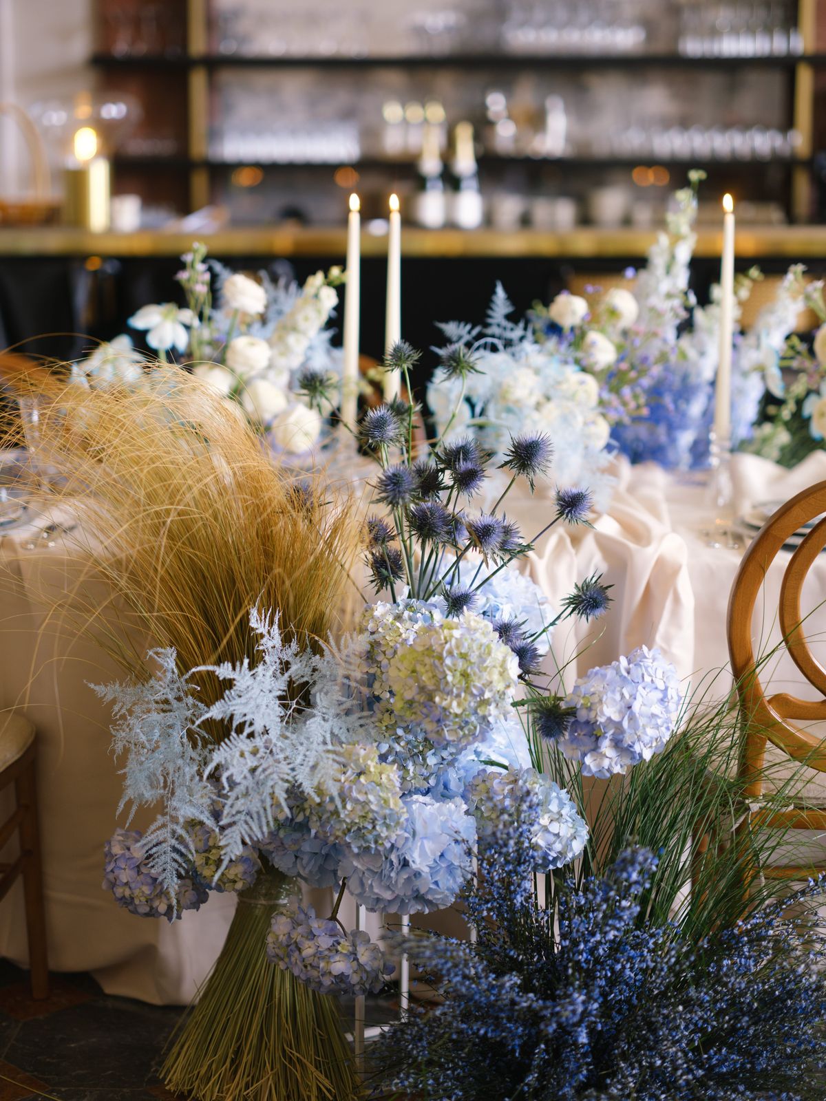 Pale blue hydrangea, eryngium thistle and delphinium arrangements with ivory tapers in château dining room