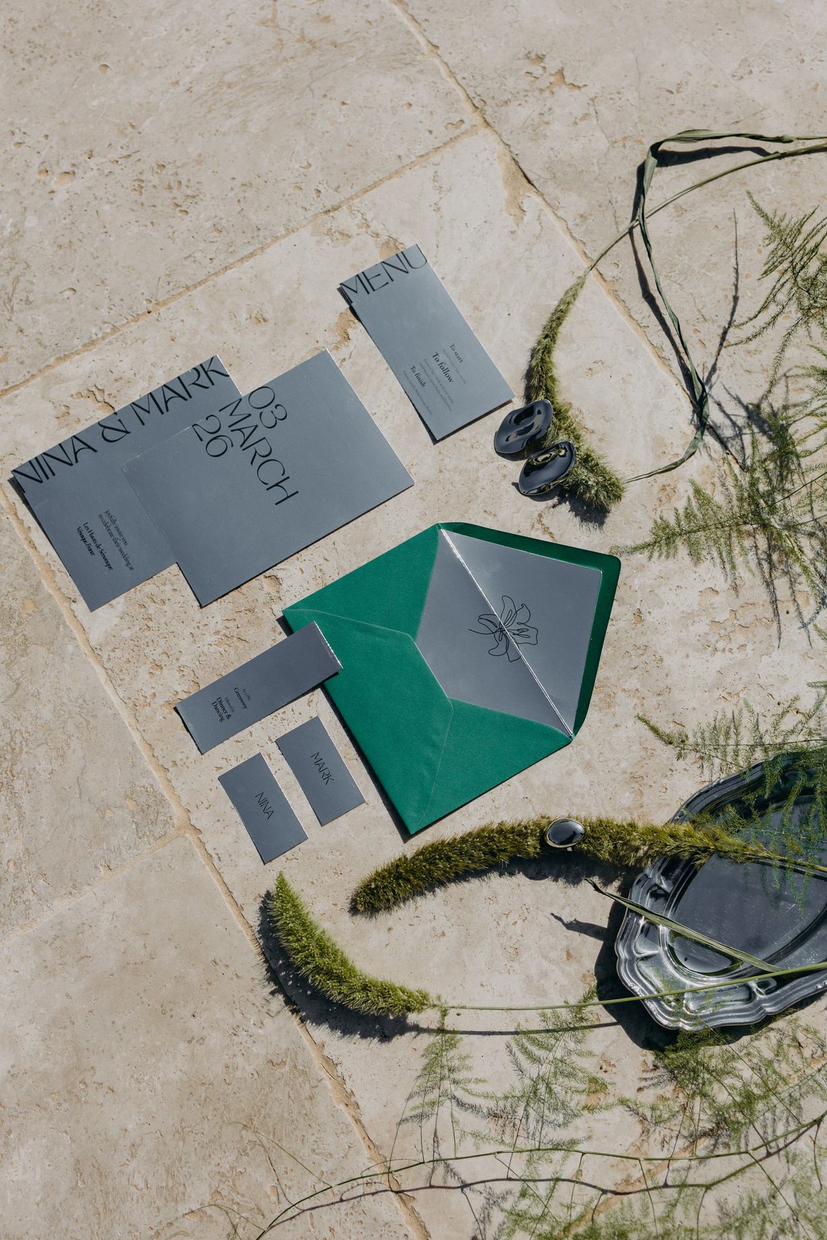 Grey and green invitation suite with moss and foliage, flat lay
