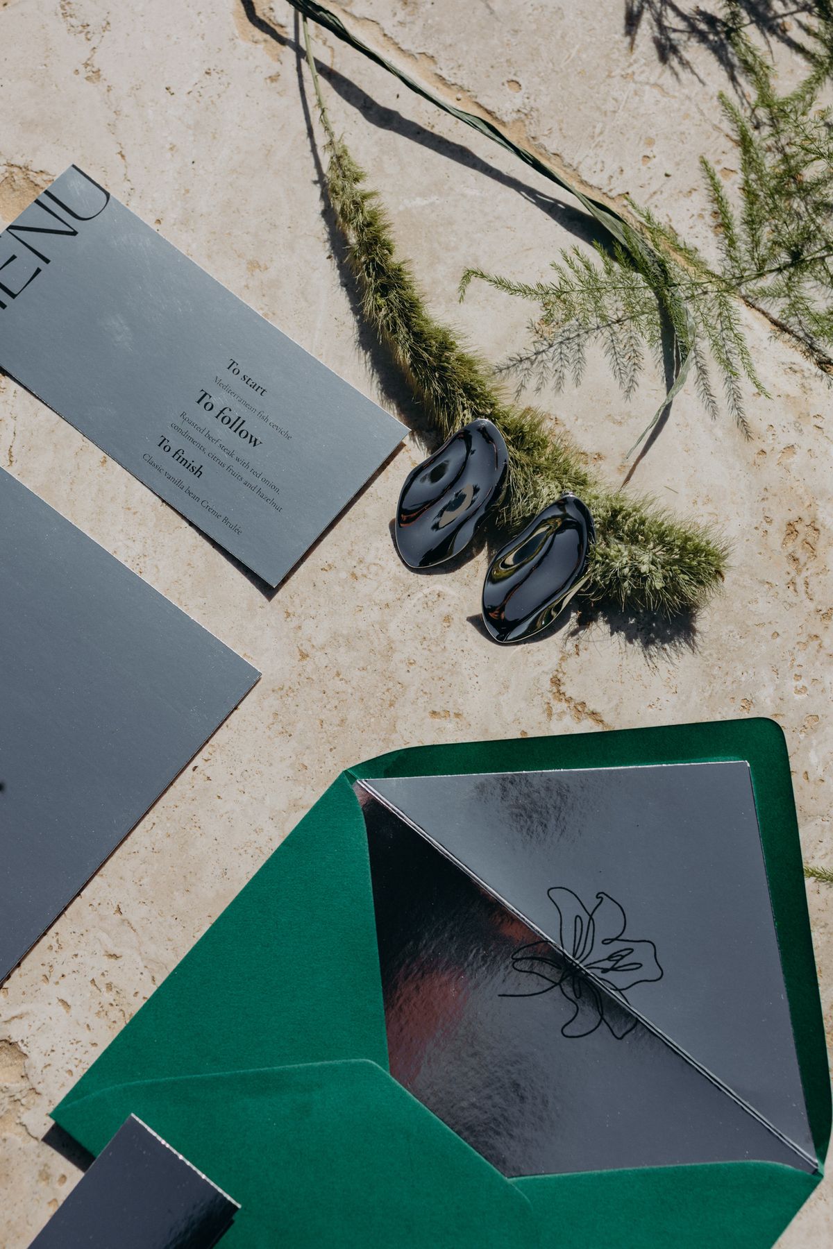 Invitation suite detail with emerald envelope and pressed foliage