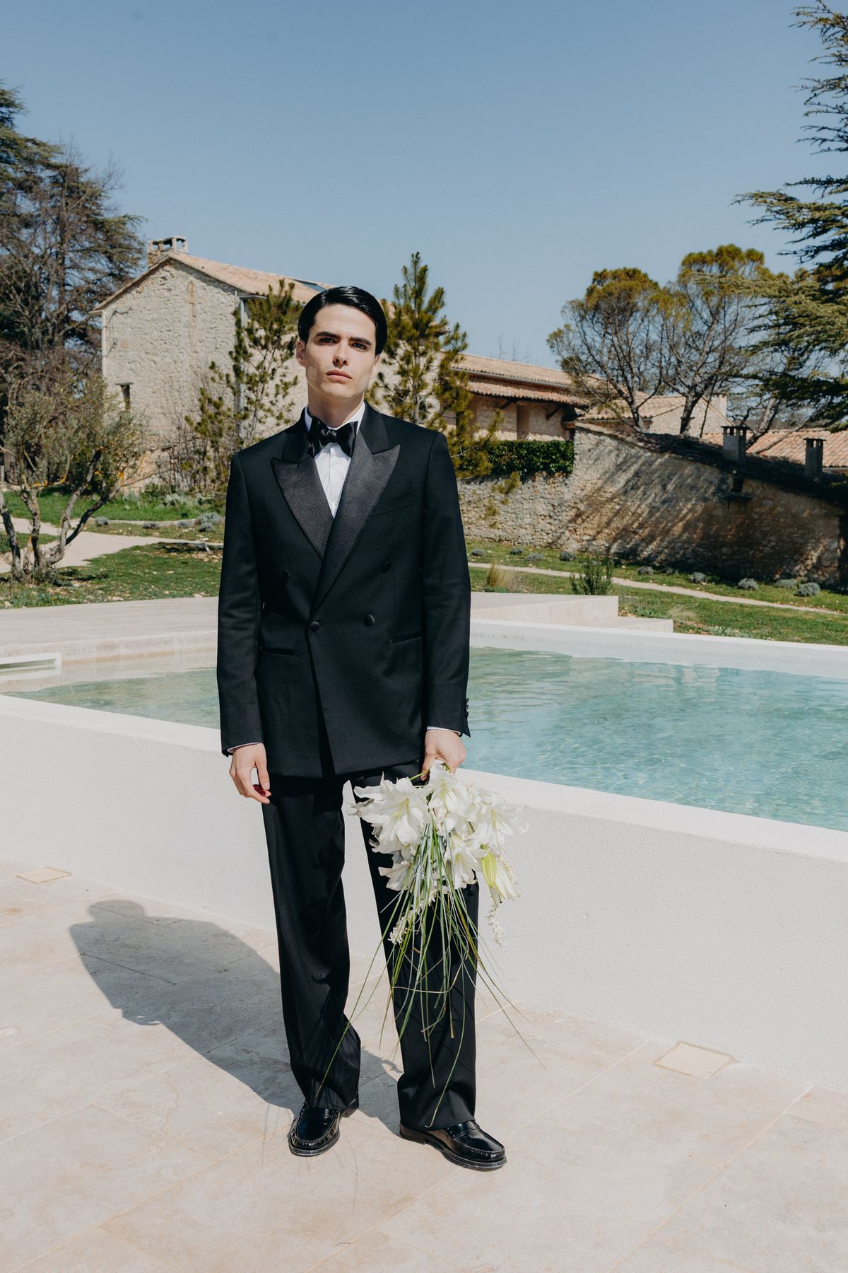 Groom holding a white bouquet beside the pool