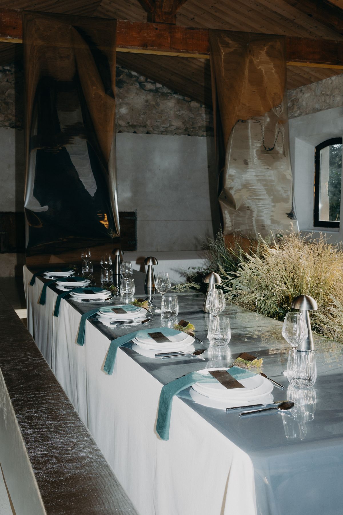 Long reception table with chrome surfaces and grasses in the former barn