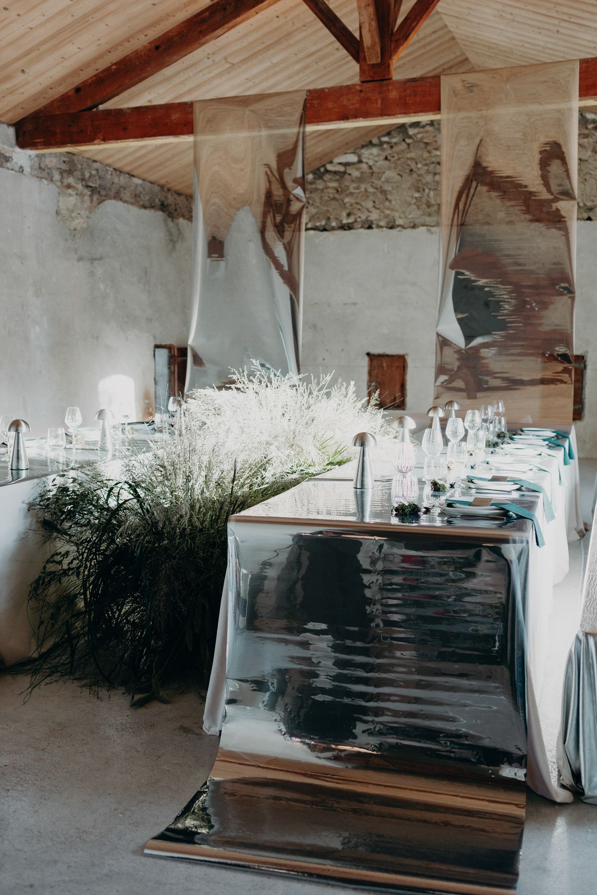 Reception table laid with silver and glass under the barn roof