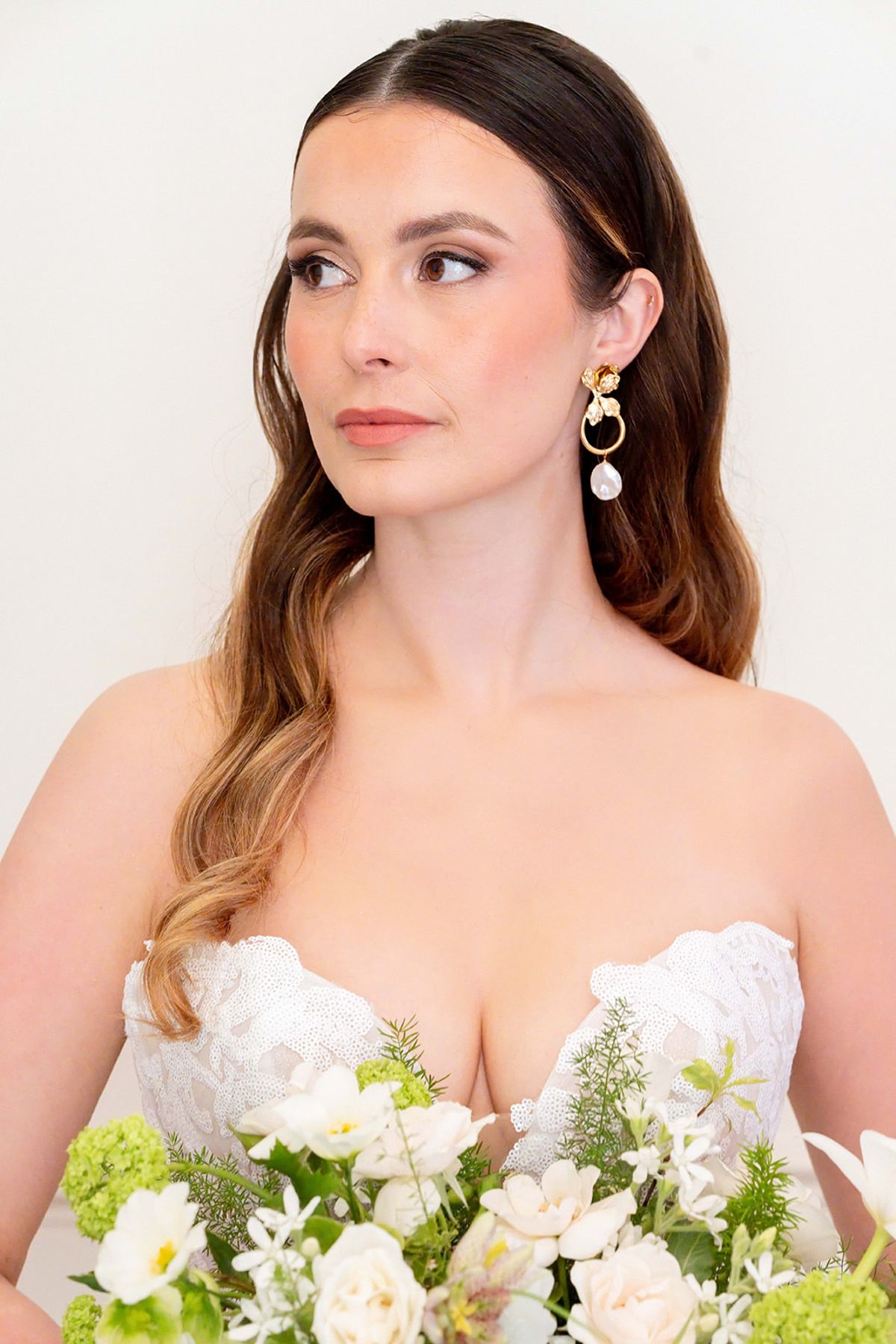 Close portrait of the bride in a strapless lace gown holding a green and cream bouquet