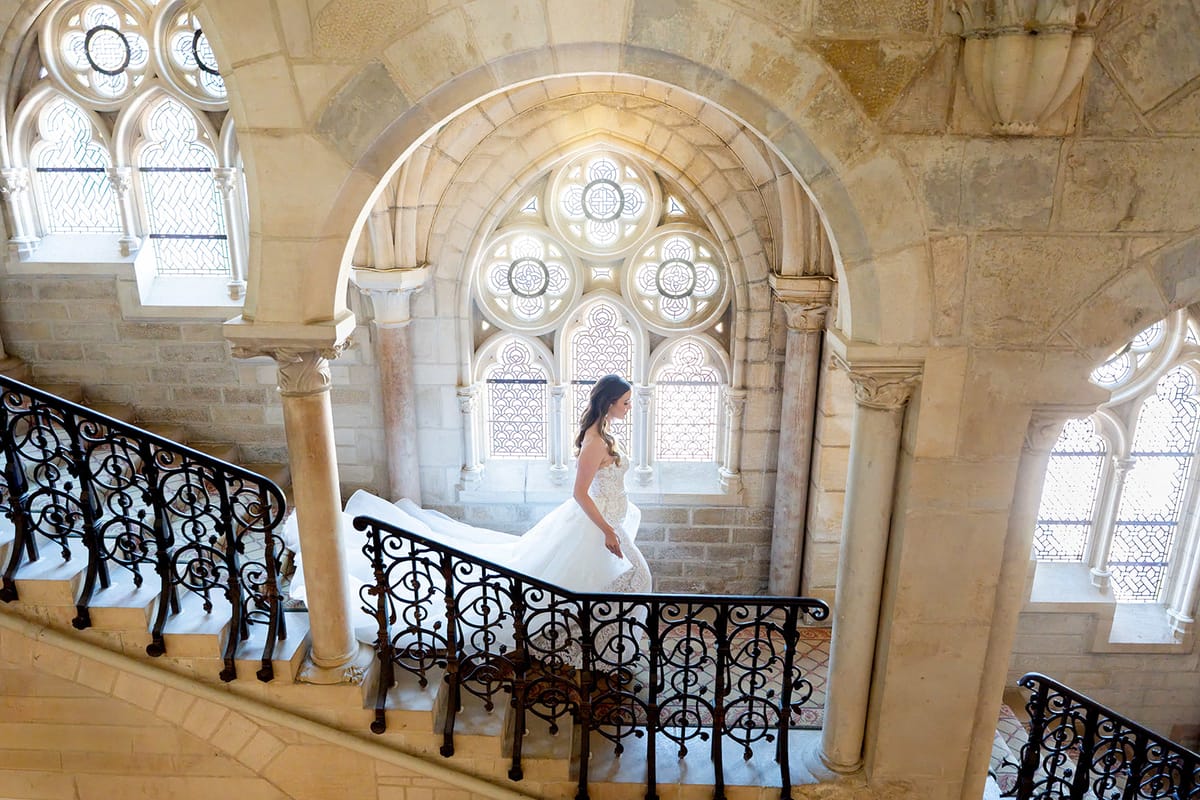 The bride on the abbey's stone staircase beneath a stained glass window