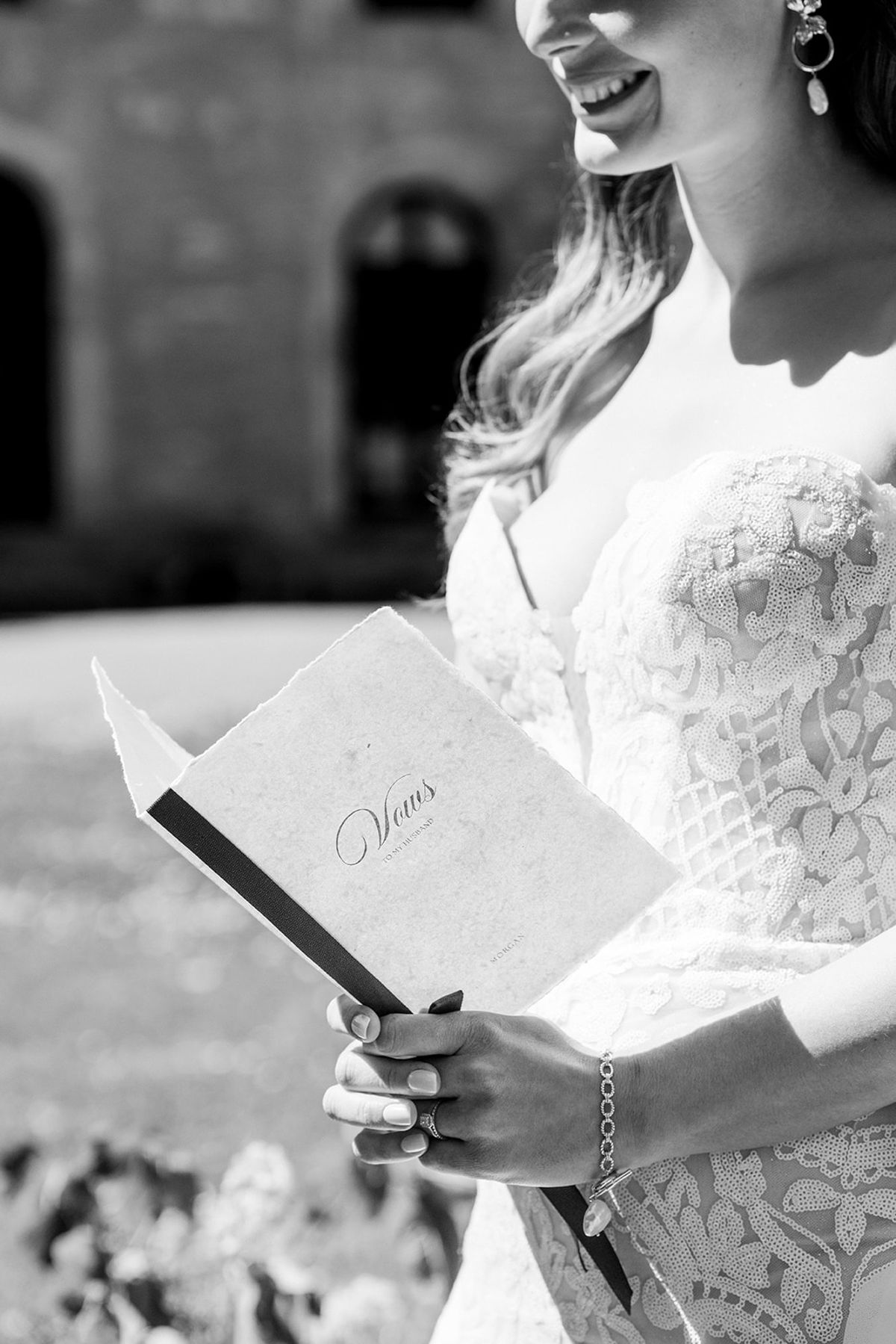 Black and white detail of the bride holding her vow book in a lace gown