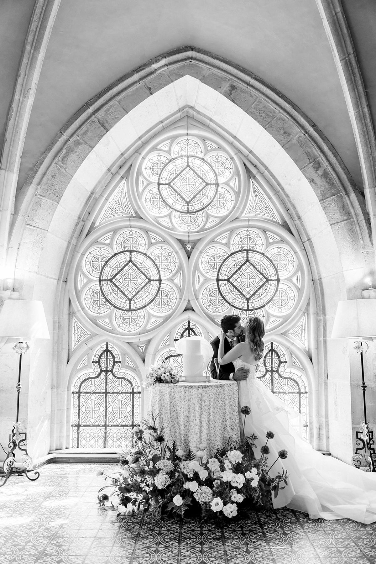 Black and white view of the couple by the cake table in the abbey chapel