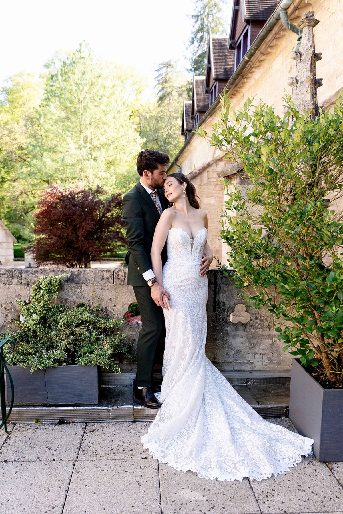 The couple beside a stone wall and potted greenery at the abbey