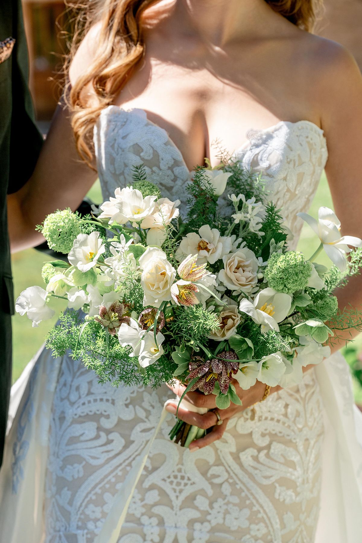 The bridal bouquet in green and cream, held against the gown's textured bodice