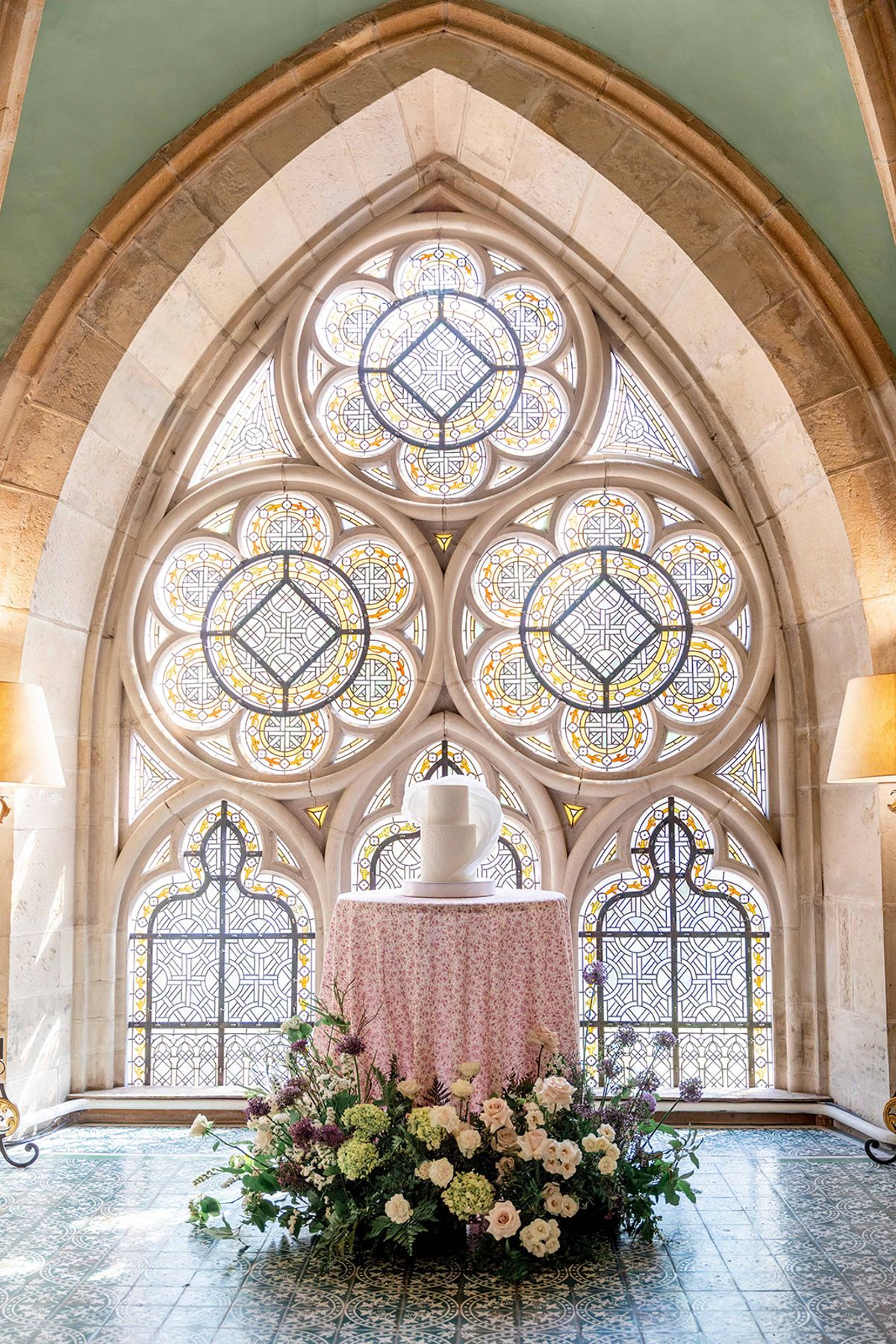 The sculptural white wedding cake on a floral cloth beneath the abbey's rose window
