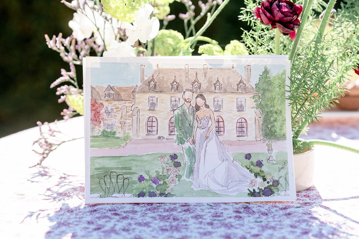 A watercolour painting of the couple in front of the abbey, propped on a patterned cloth