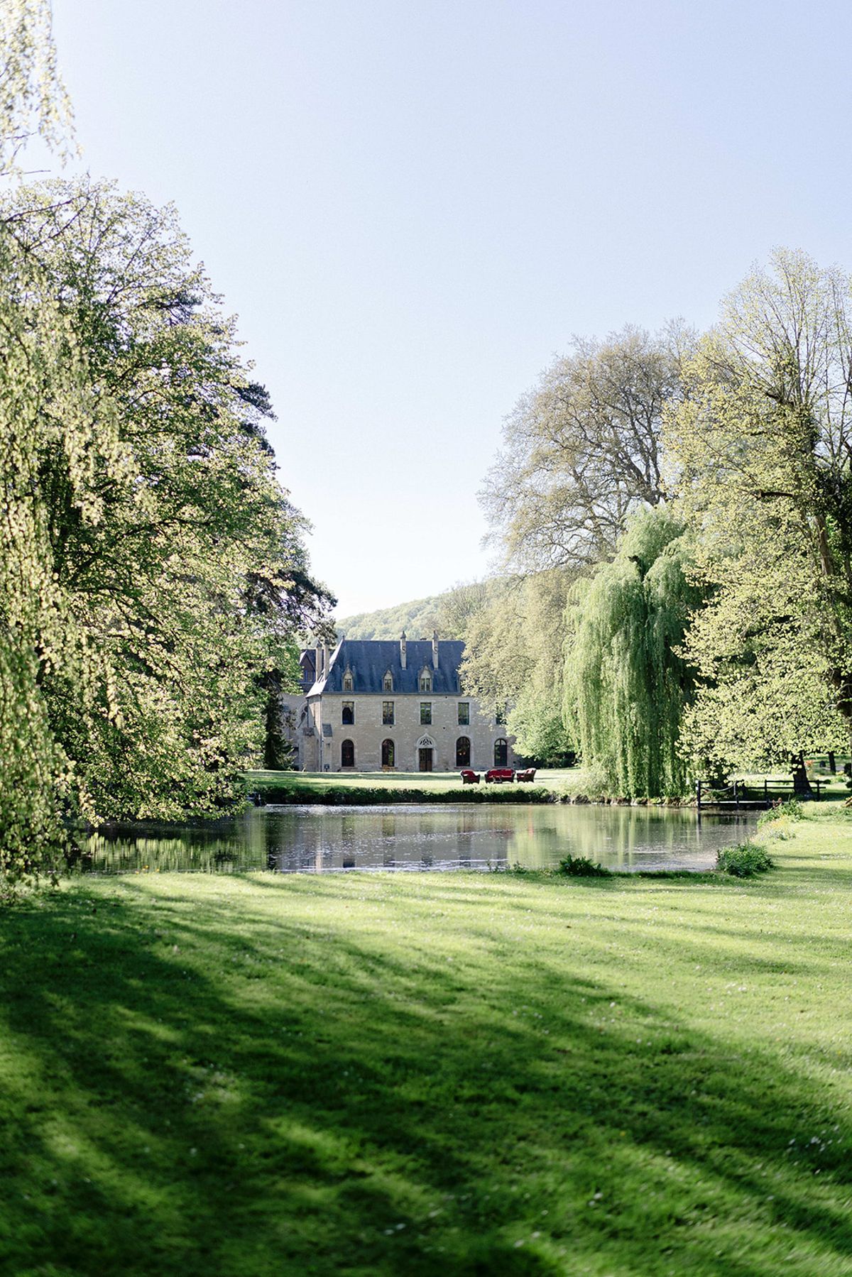 Abbaye de la Bussiere seen across its lake, with willows and lawns in late spring