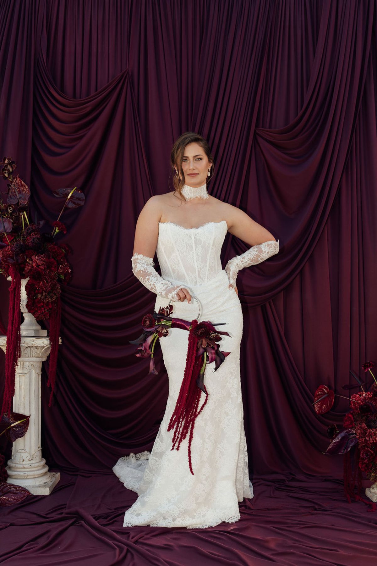 Styled shoot models Harper and Liam: the bride outdoors against a burgundy drape, bouquet in hand, Chateau de Mirambeau, spring editorial