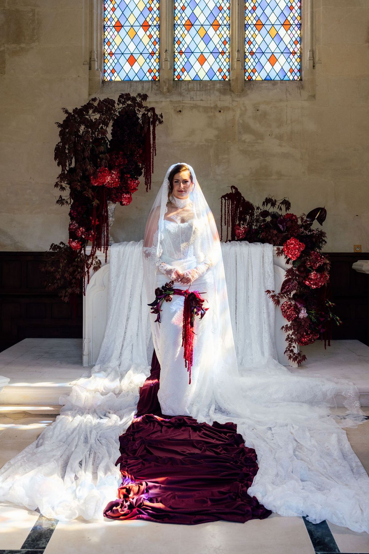 Styled shoot models Harper and Liam: the bride alone at the altar in her veil, stained glass overhead, Chateau de Mirambeau, spring editorial