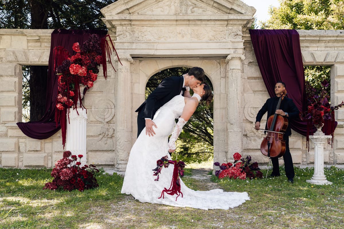 Styled shoot models Harper and Liam: the couple kissing at the archway as a cellist plays, Chateau de Mirambeau, spring editorial