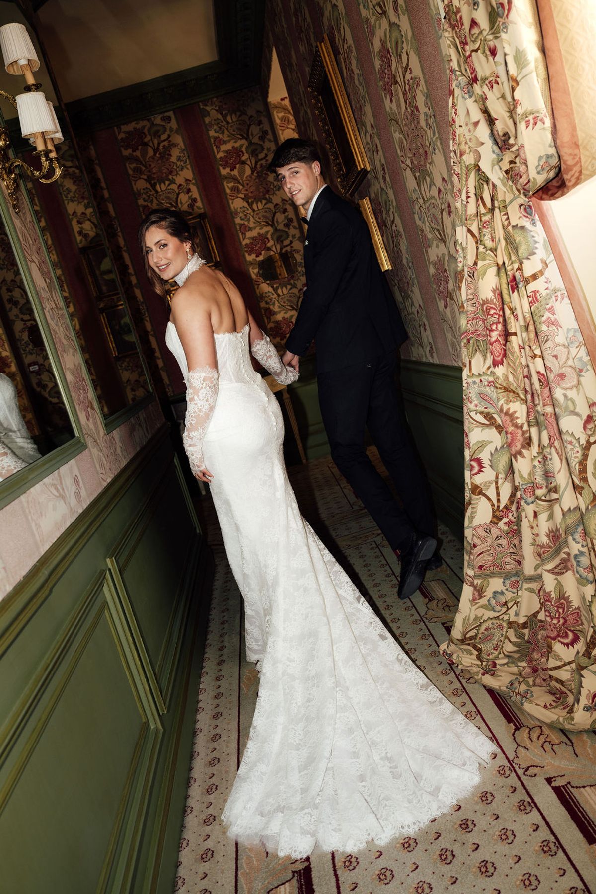 Styled shoot models Harper and Liam: the bride walking a corridor as the groom watches, Chateau de Mirambeau, spring editorial