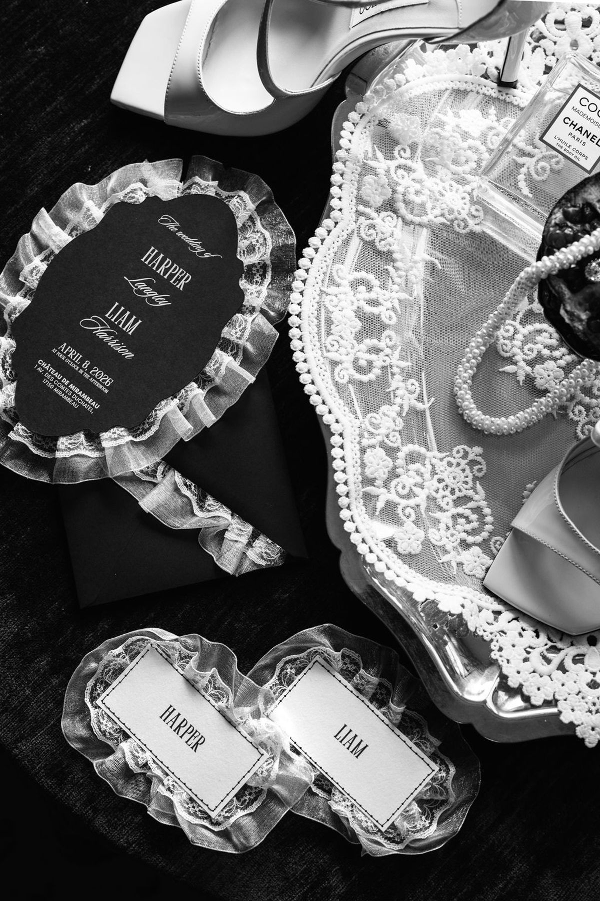 Styled shoot models Harper and Liam: black-and-white flat lay of the invitation suite, lace-trimmed place cards for Harper and Liam, heels, and perfume, Chateau de Mirambeau, spring editorial