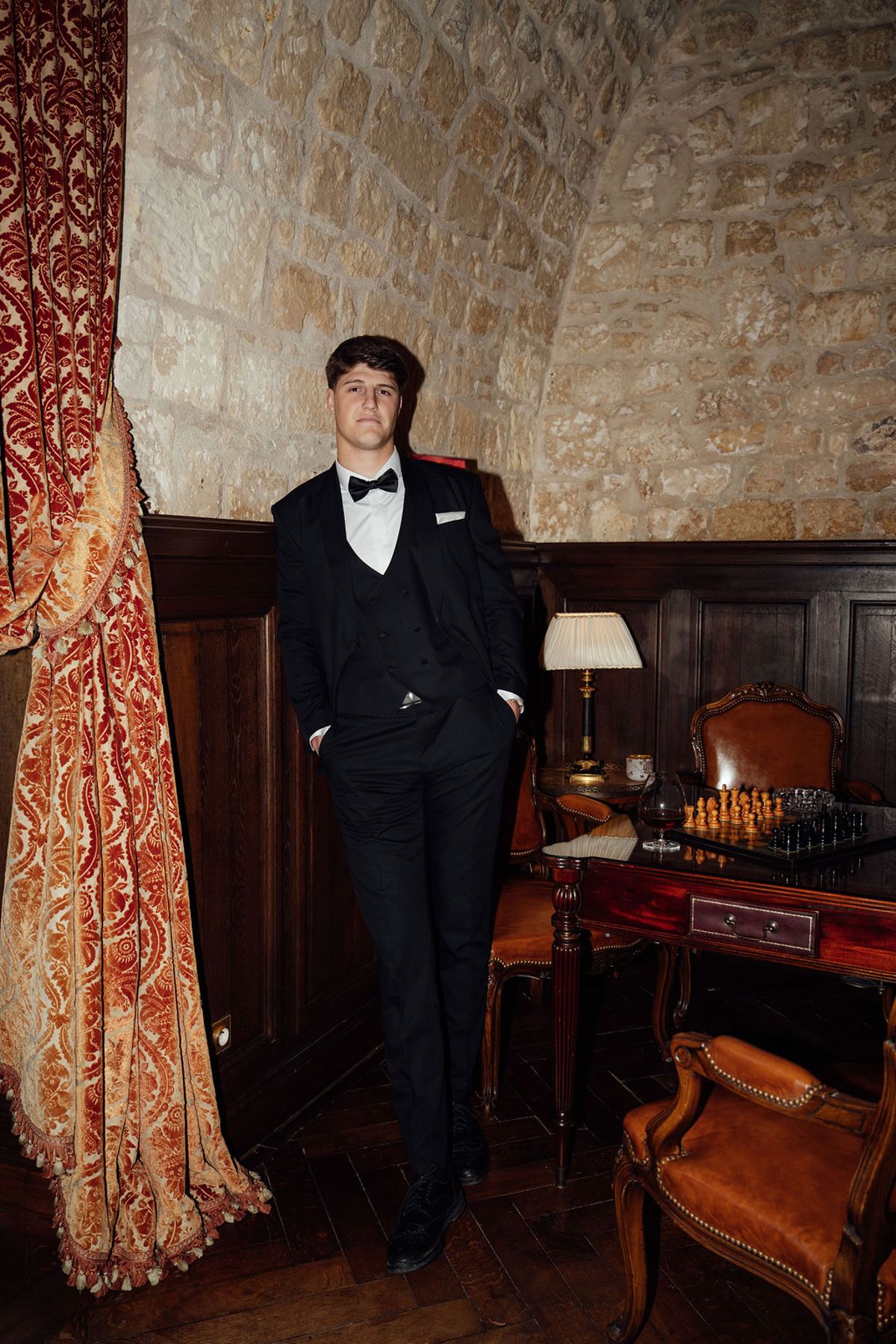 Styled shoot models Harper and Liam: the groom standing in a wood-panelled room in his tuxedo, Chateau de Mirambeau, spring editorial