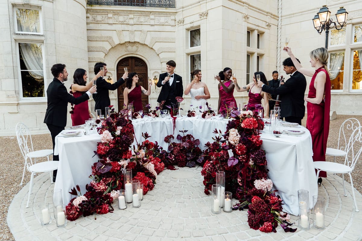 Styled shoot models Harper and Liam: the long reception table set with burgundy blooms and candlelight, Chateau de Mirambeau, spring editorial