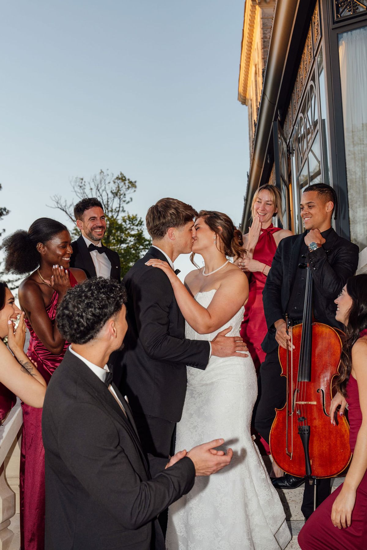 Styled shoot models Harper and Liam: the couple kissing among guests at golden hour, the cellist beside them, Chateau de Mirambeau, spring editorial