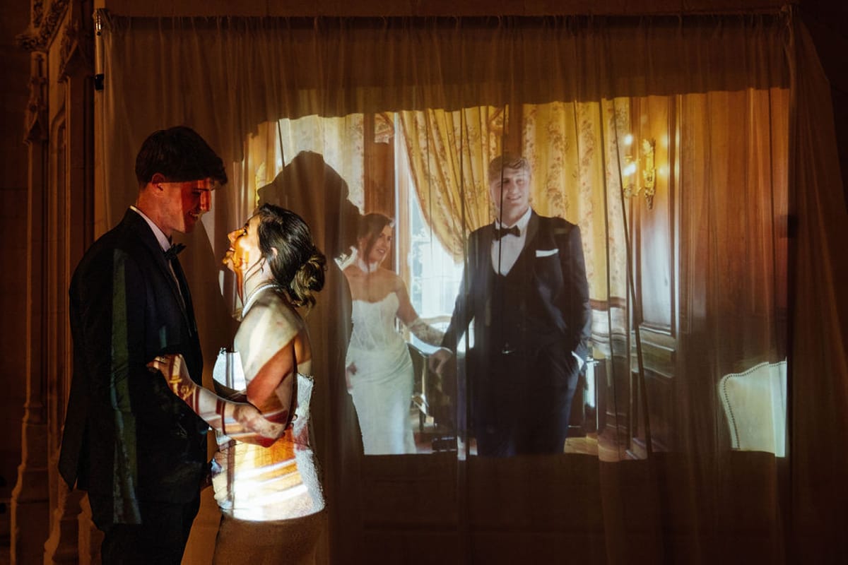 Styled shoot models Harper and Liam: a dim evening view of the couple through a chateau window, Chateau de Mirambeau, spring editorial