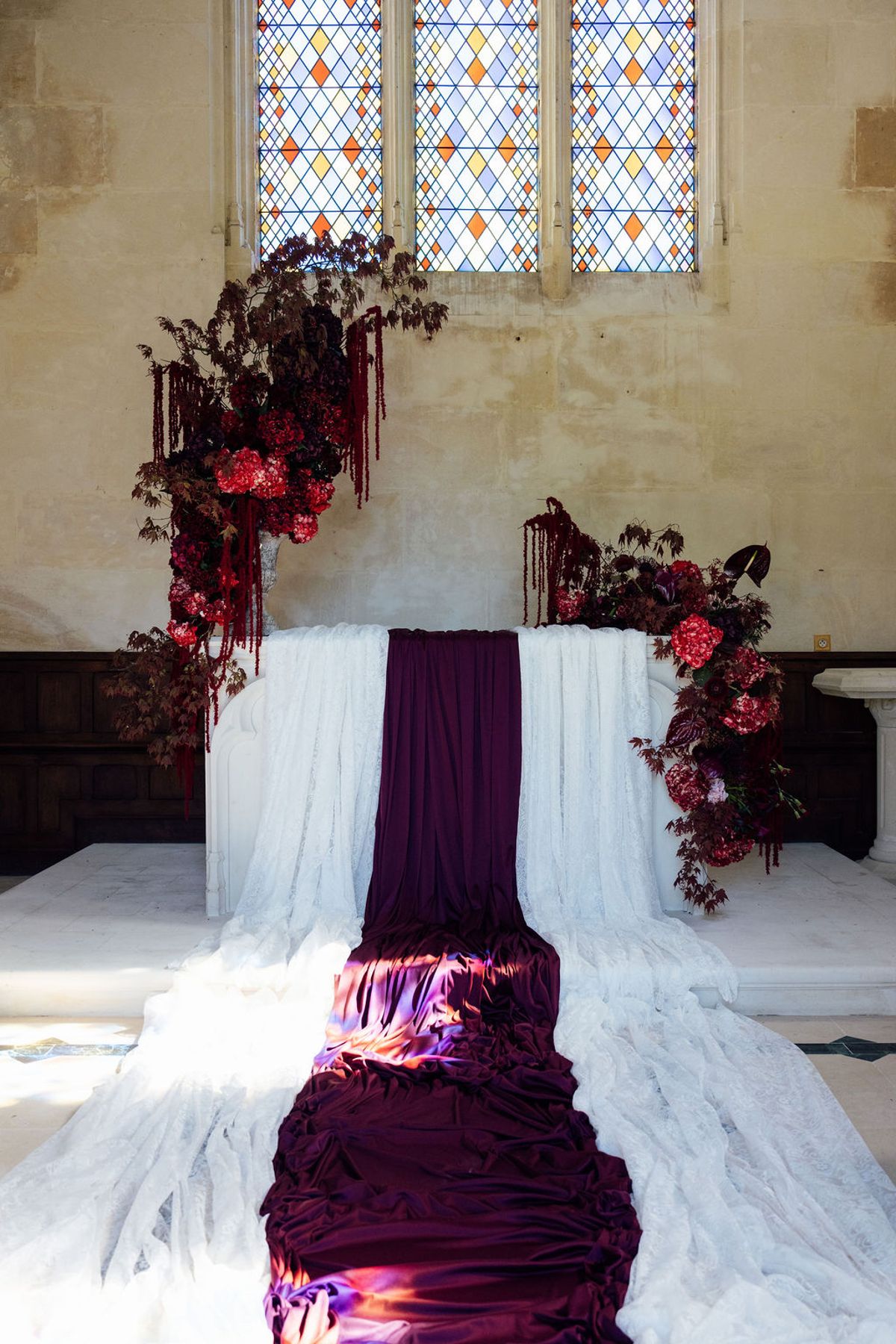 Styled shoot models Harper and Liam: the chapel altar dressed in white linen and burgundy blooms, before the ceremony, Chateau de Mirambeau, spring editorial