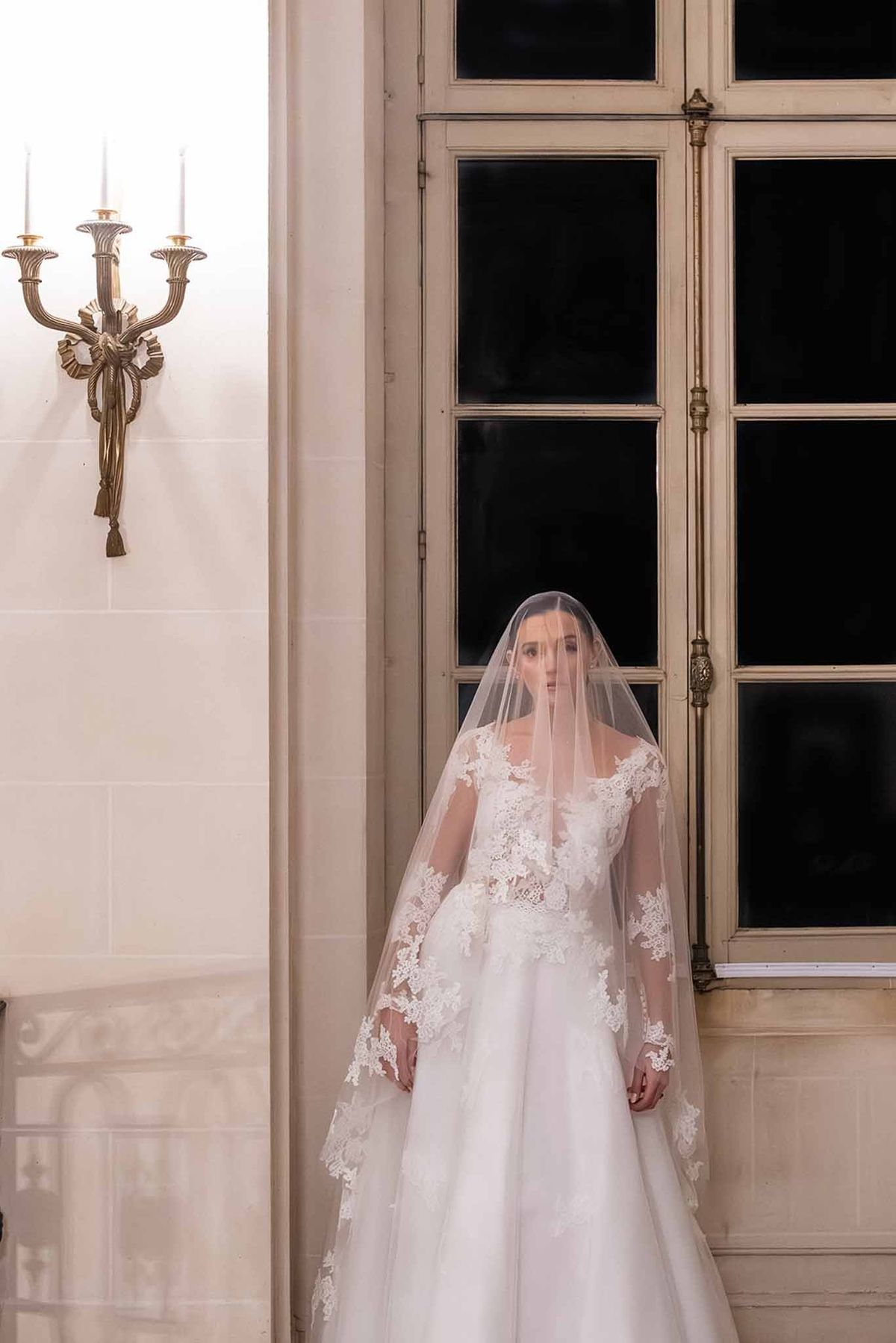 Bride in lace gown with cathedral veil at Chateau du Terral window