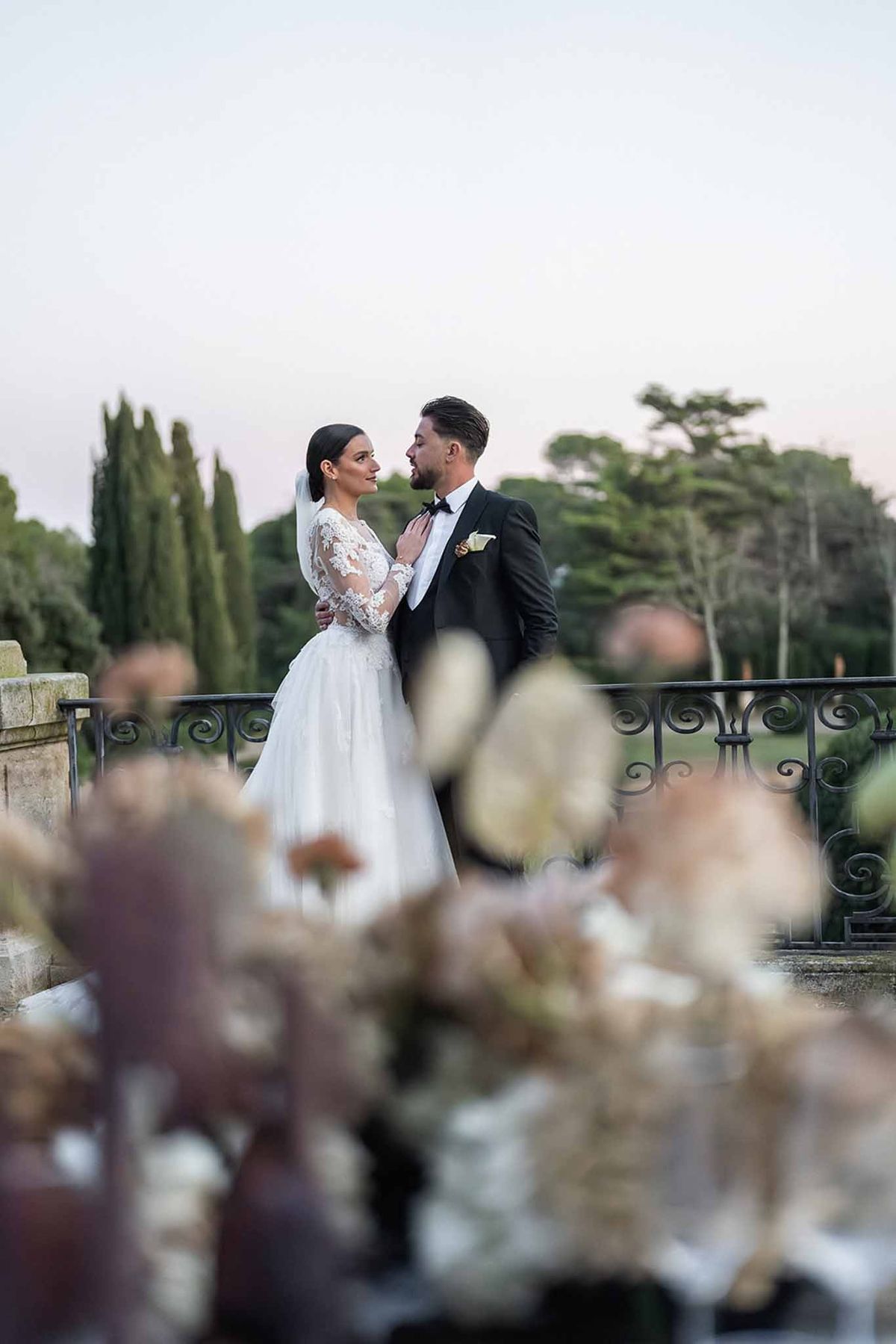 Couple embracing on balcony at dusk at Chateau du Terral through floral arrangement