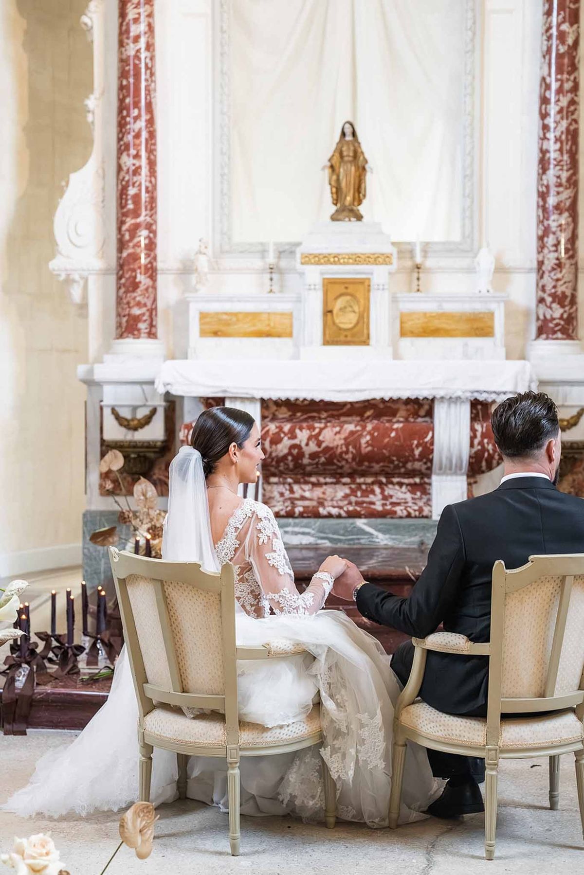 Couple seated holding hands at chapel altar at Chateau du Terral from behind