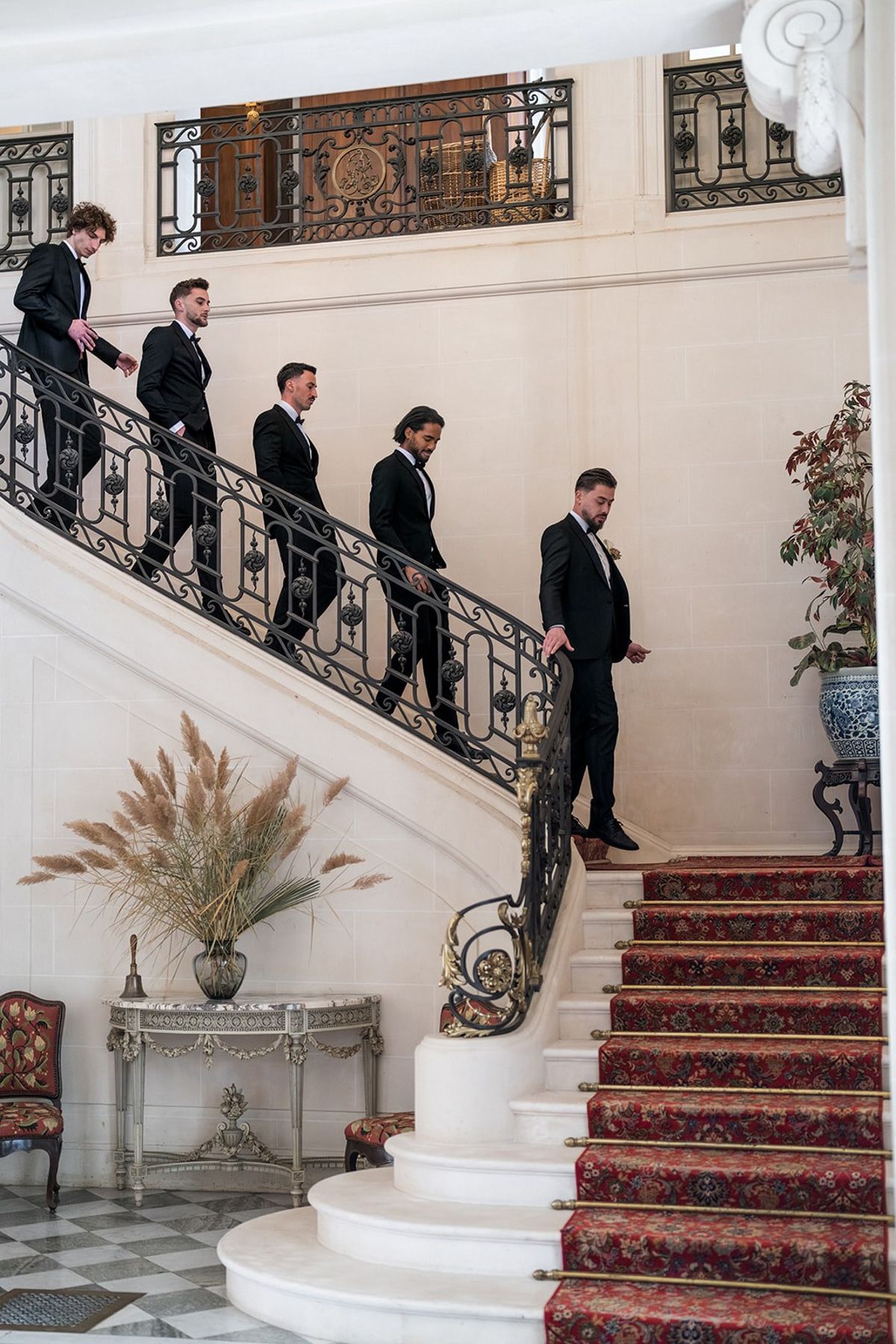 Groom and groomsmen in tuxedos descending grand stone staircase at Chateau du Terral
