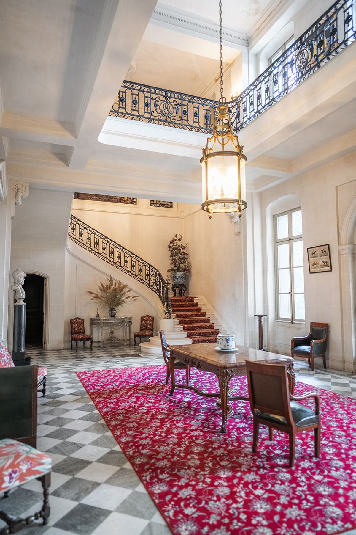 Grand entrance hall with curved staircase and crimson rug at Chateau du Terral