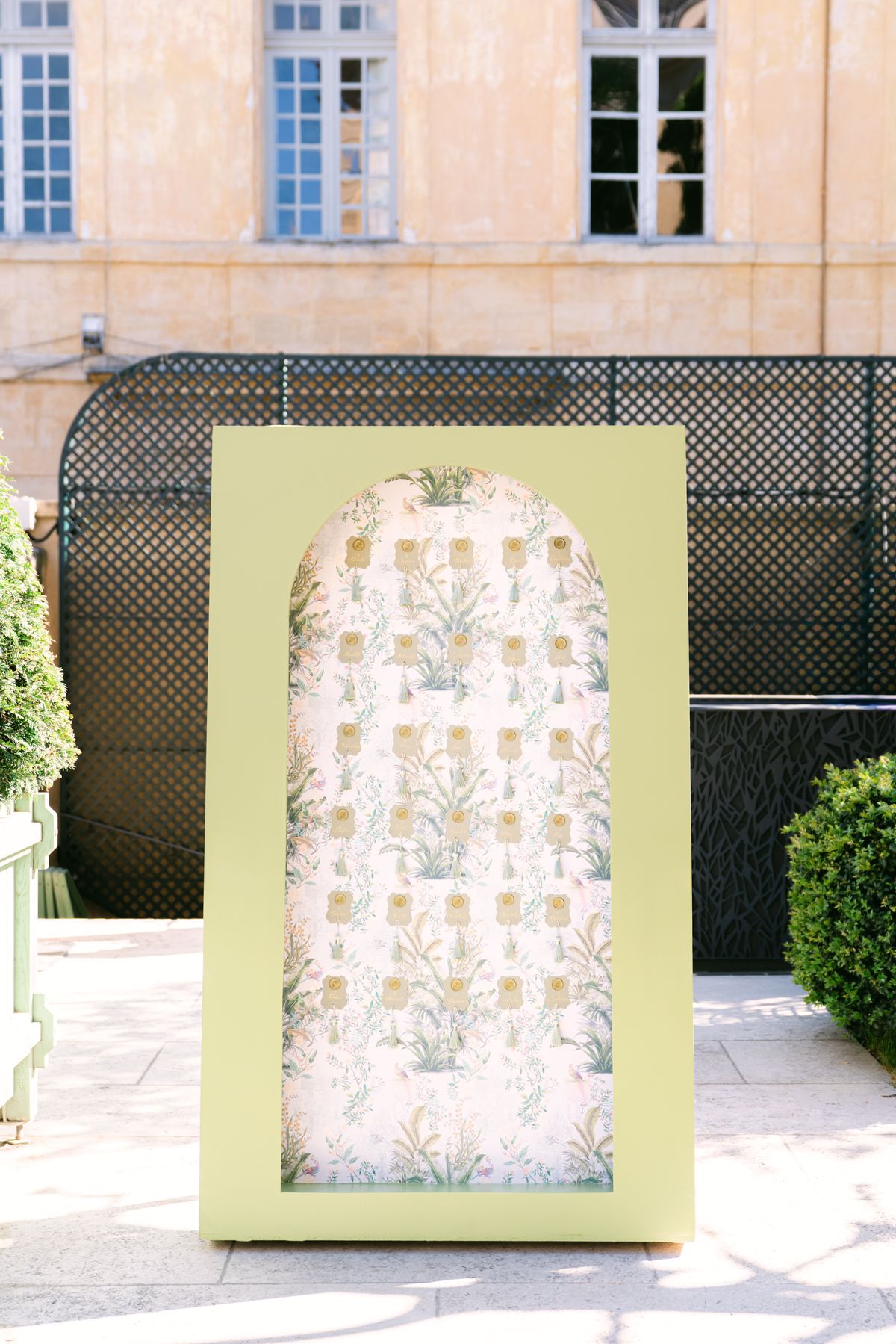 Arched botanical-print panel standing against dark iron gates