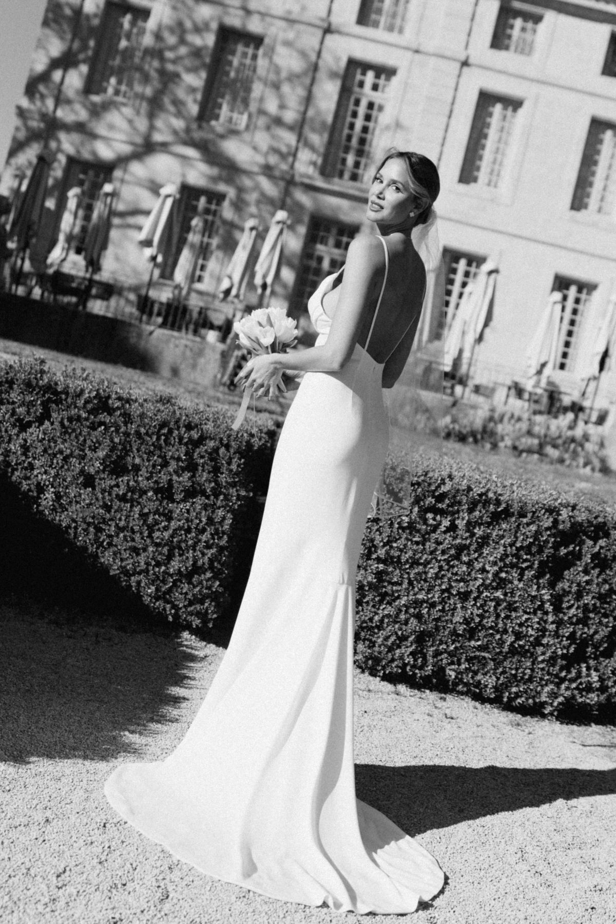 Black and white portrait of the bride beside a clipped hedge with the chateau behind