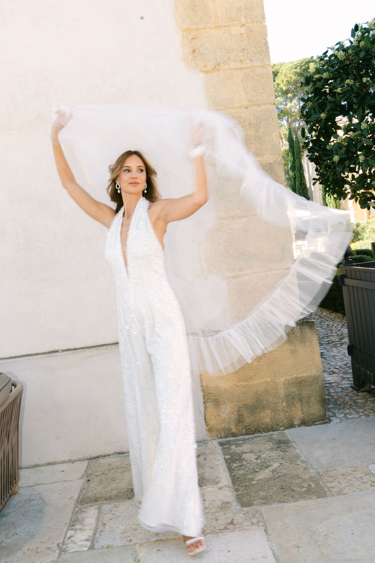 Bride in a sequinned halter jumpsuit holding a veil above her head