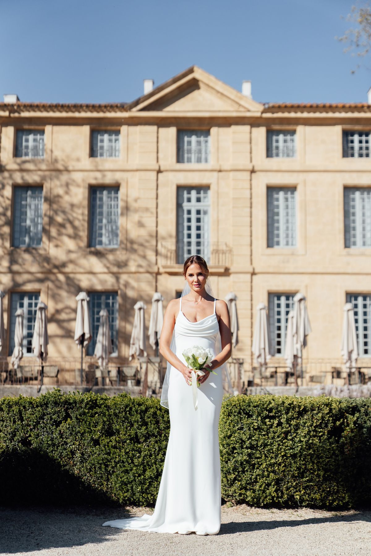 Bride in a slip gown standing before the facade of Chateau de la Gaude