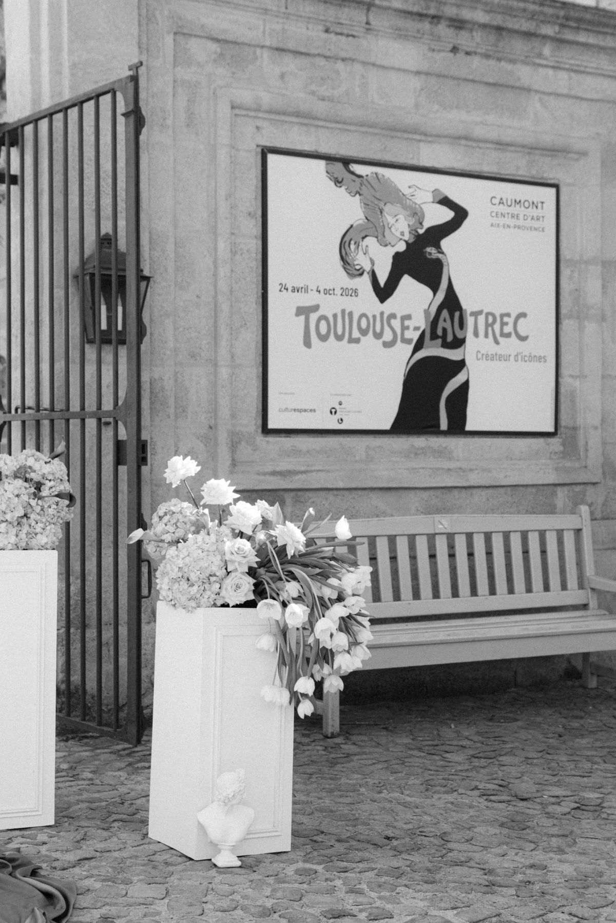 Black and white view of the Caumont Centre d’Art entrance with a bench and white florals