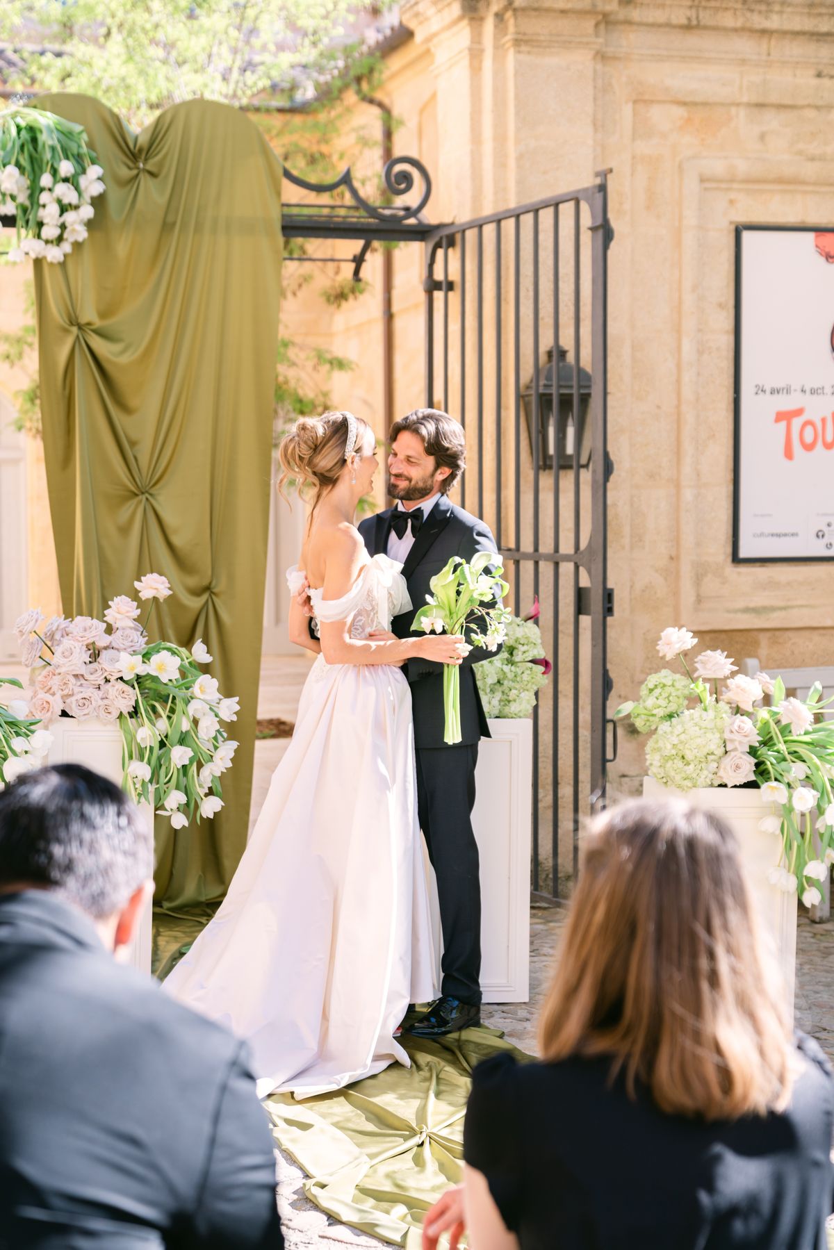Couple embracing beneath the olive-green draped gateway at the end of the ceremony