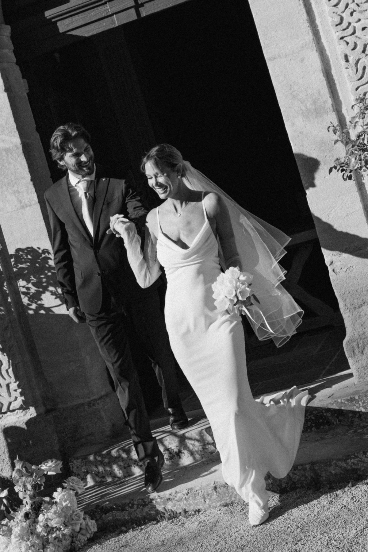 Black and white view of the couple walking together beneath a stone arcade