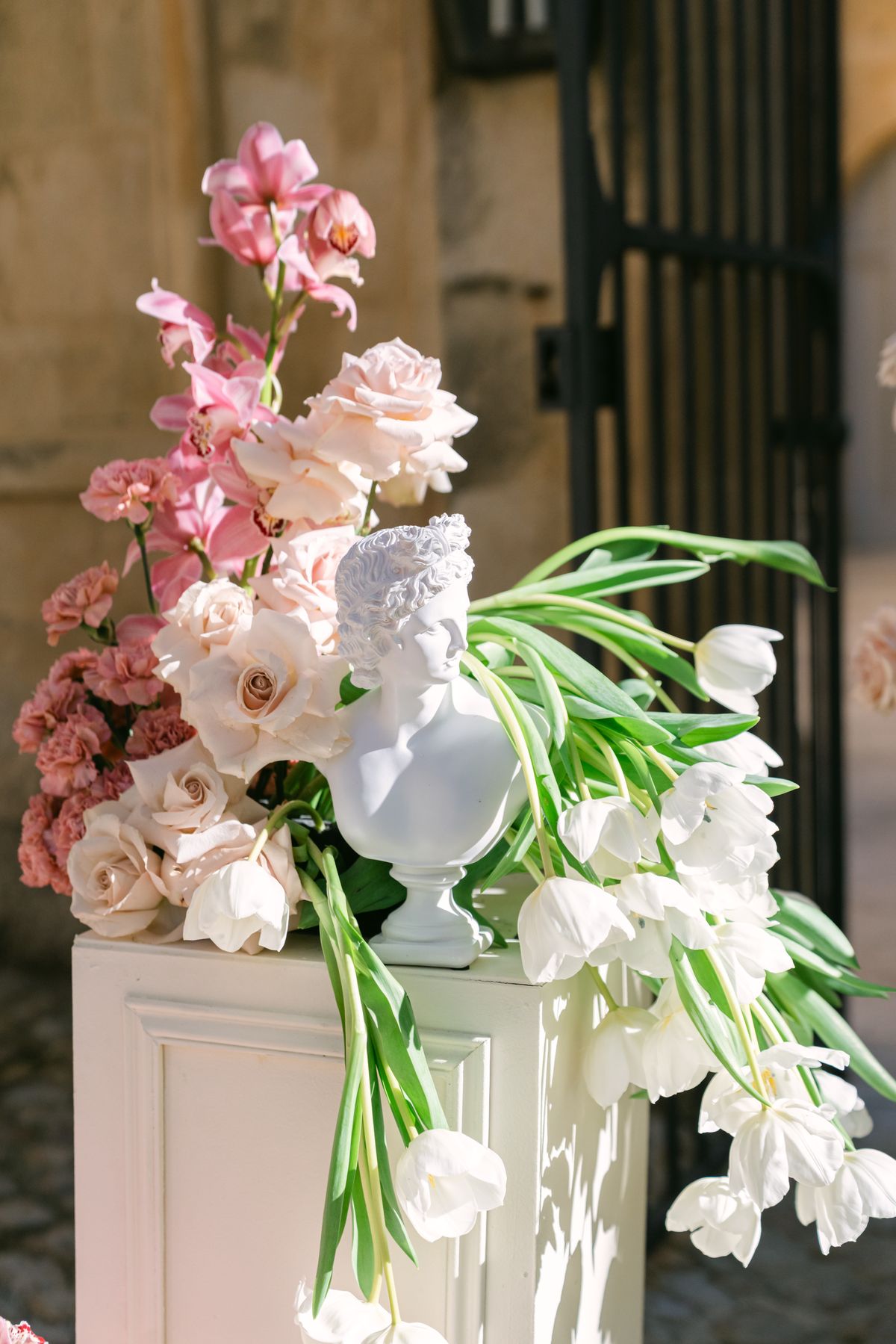 Pink and white floral arrangement with a white bust sculpture on a white plinth