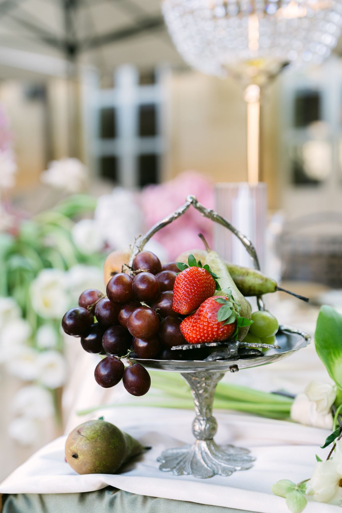 Silver comport of grapes, strawberries and a pear on a dressed table
