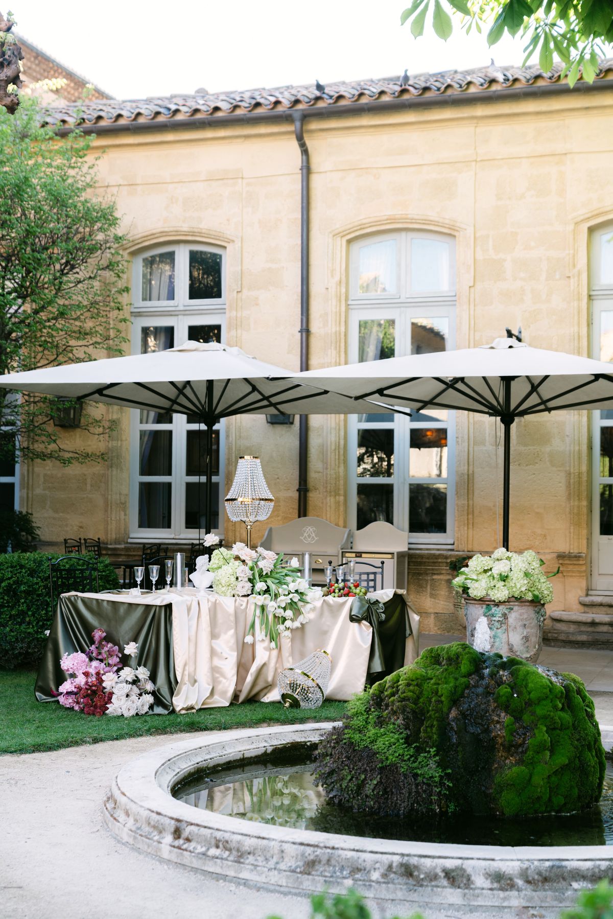 Garden dining setup with cream parasols and dressed tables beside a pond