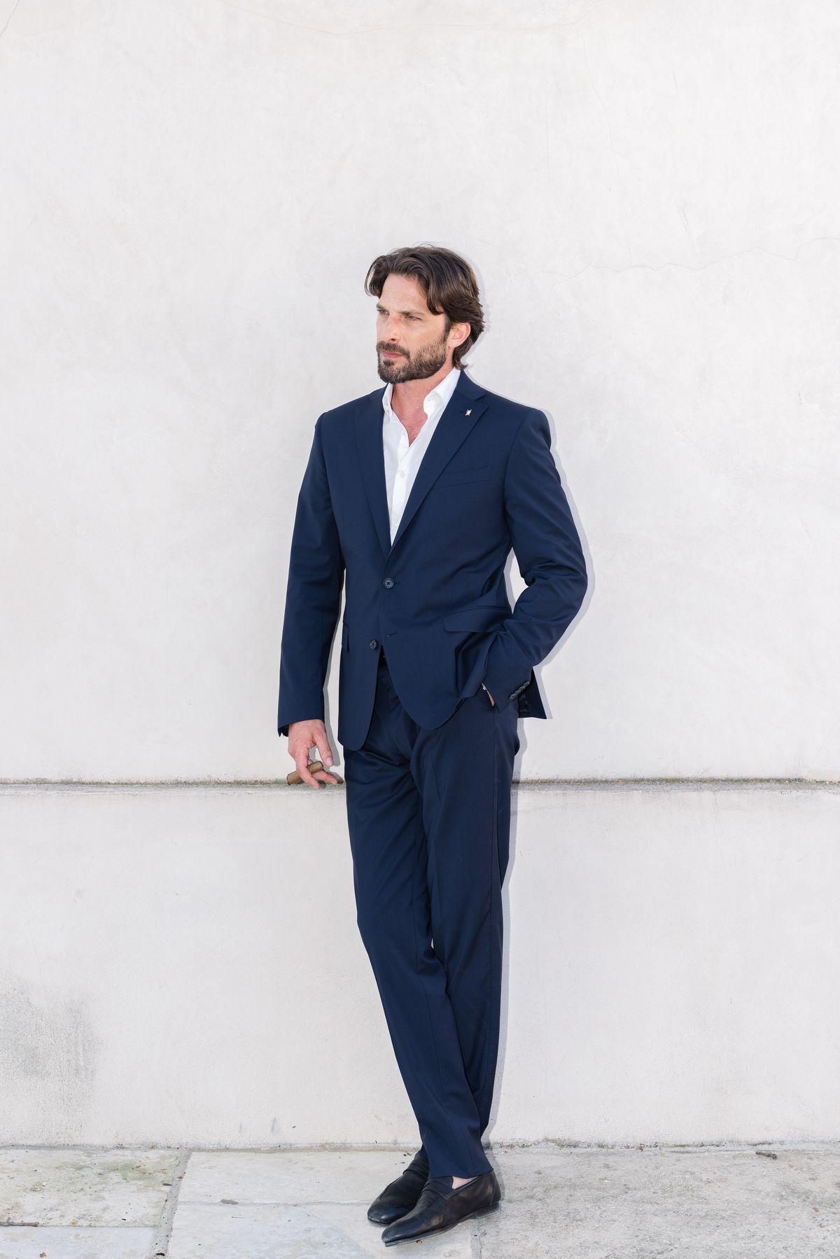 Groom in a navy suit standing against a white wall