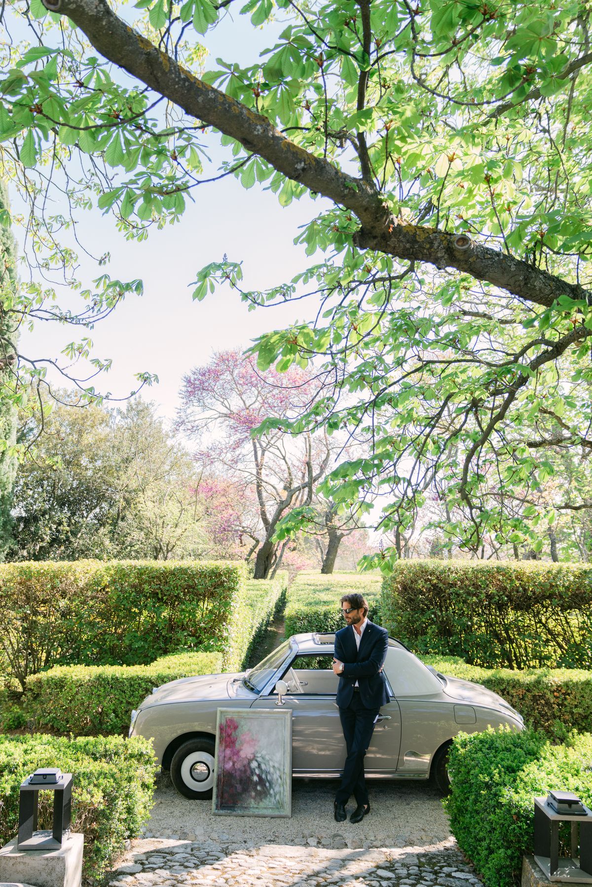 Groom standing beside a vintage car with a live-painted canvas on the gravel