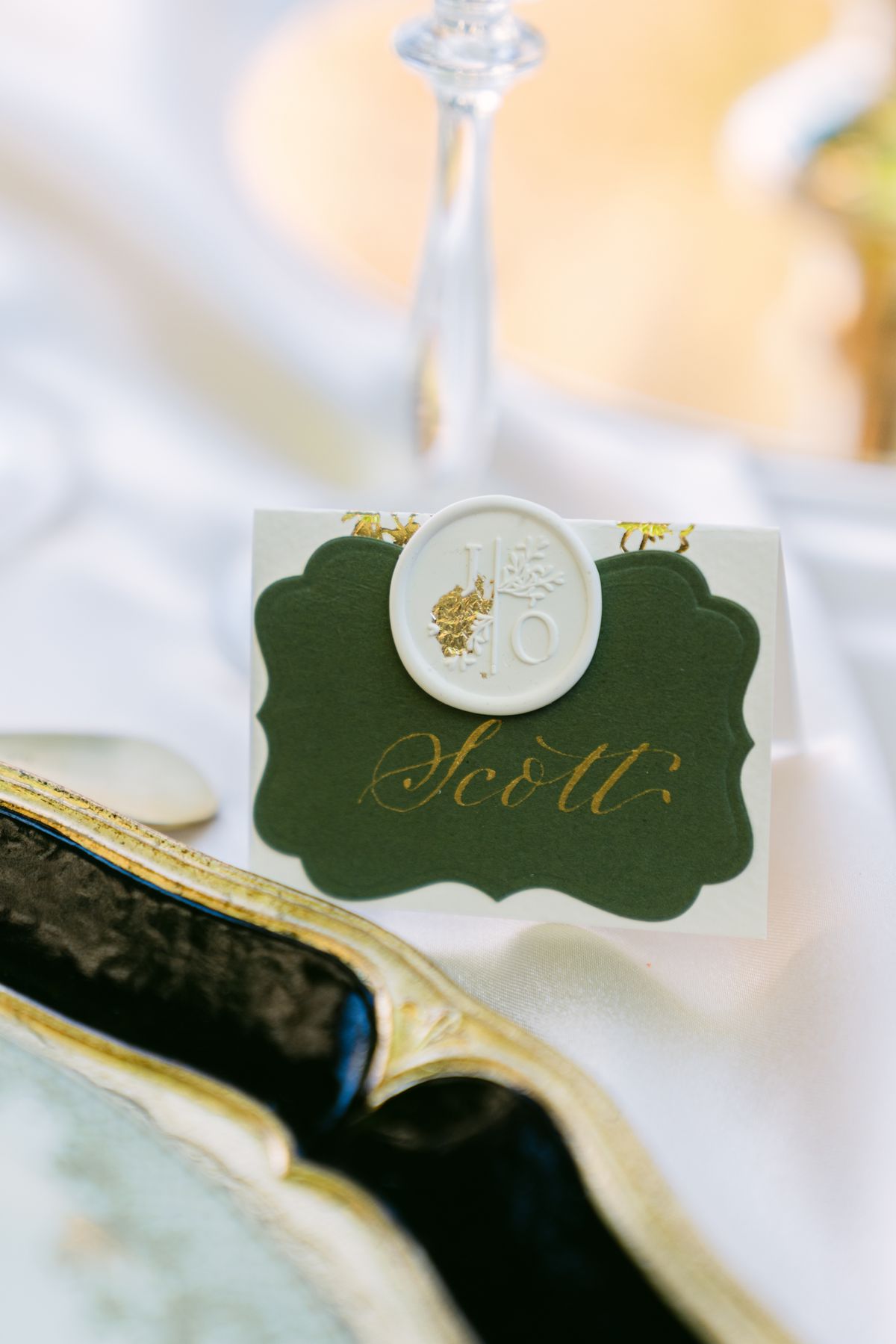 Olive-green place card with a gold wax seal resting on a charger plate