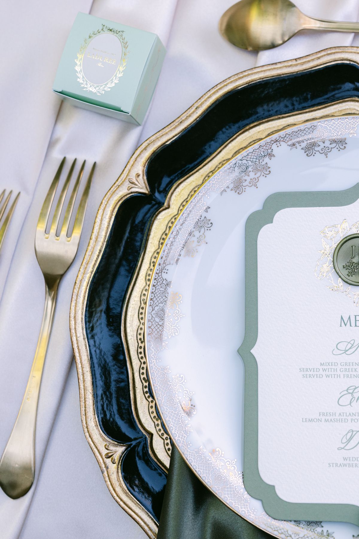Place setting with gold cutlery, scalloped charger and a mint green favour box