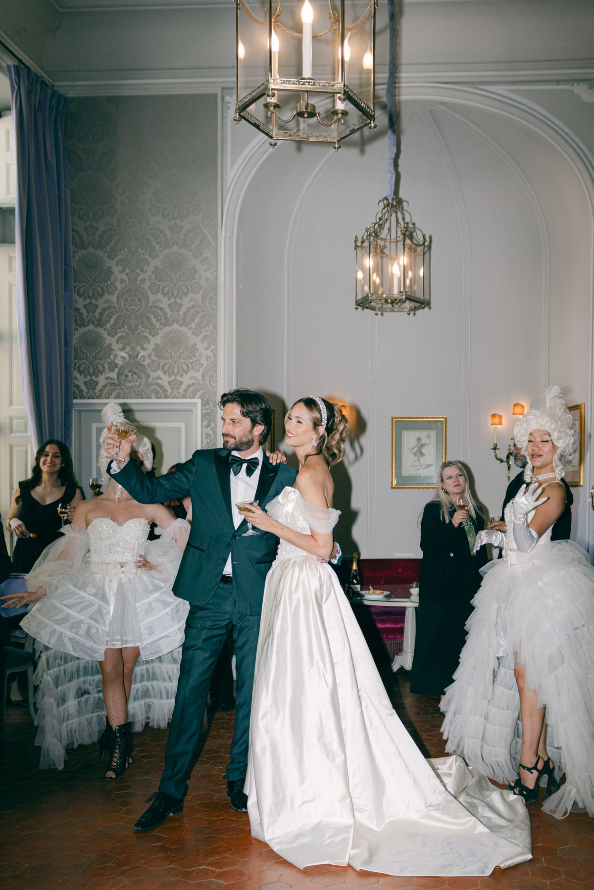 Couple raising a toast beneath hanging lanterns in a panelled salon