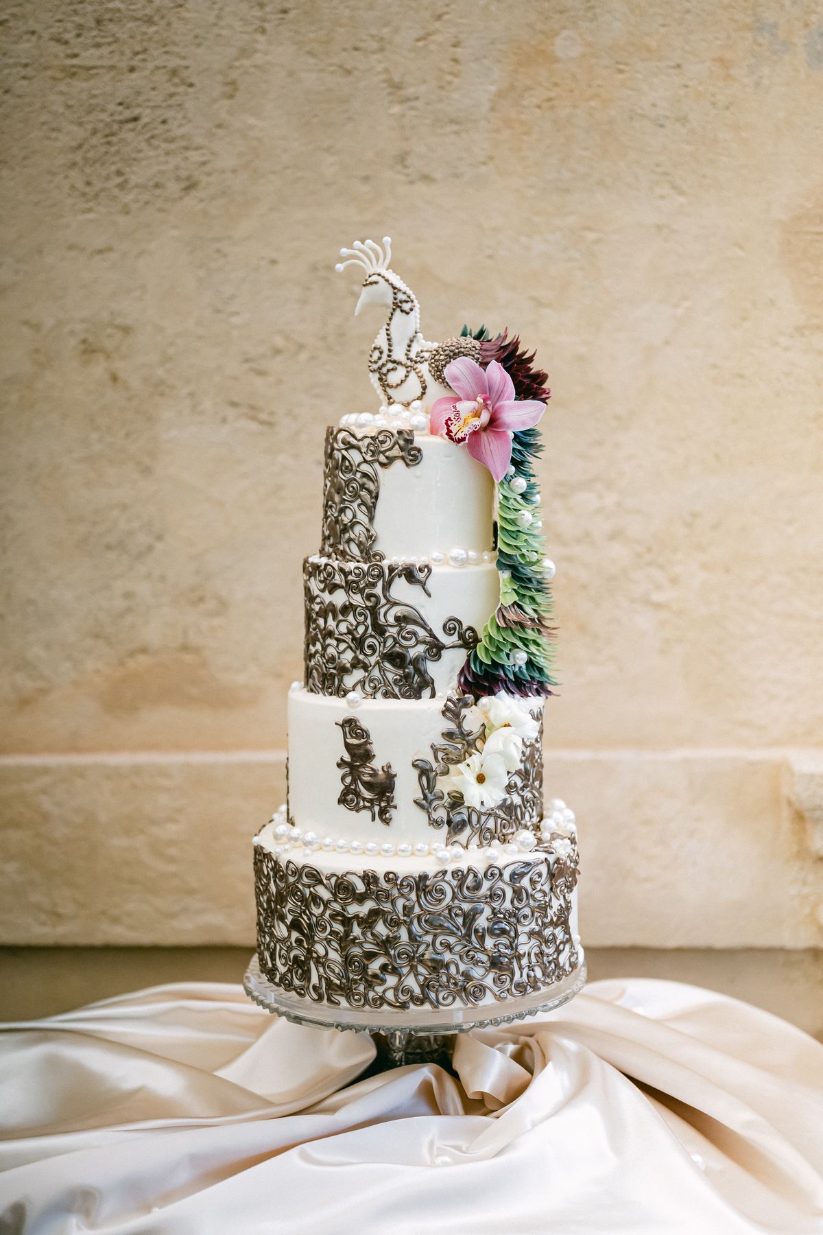 Tiered wedding cake with baroque scrollwork and an orchid on olive silk