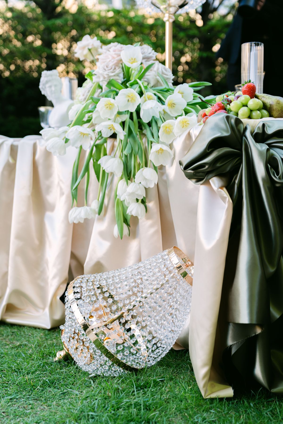 White tulips and a crystal chandelier resting on olive silk beside a dressed table