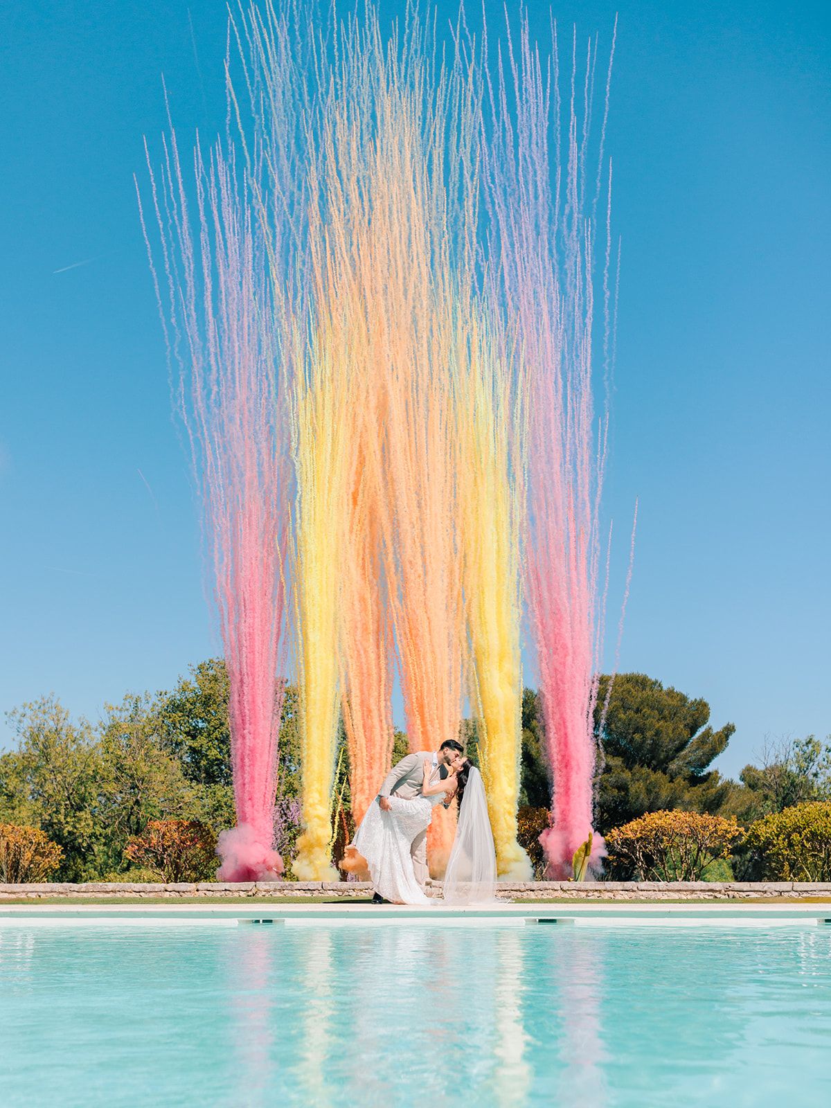 Bride and groom before the coloured water jets arcing across the pool