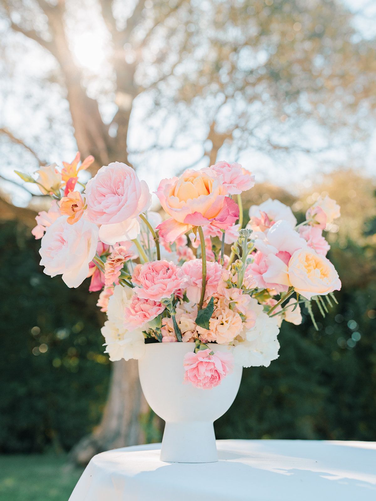 Blush and pink arrangement in a white footed urn