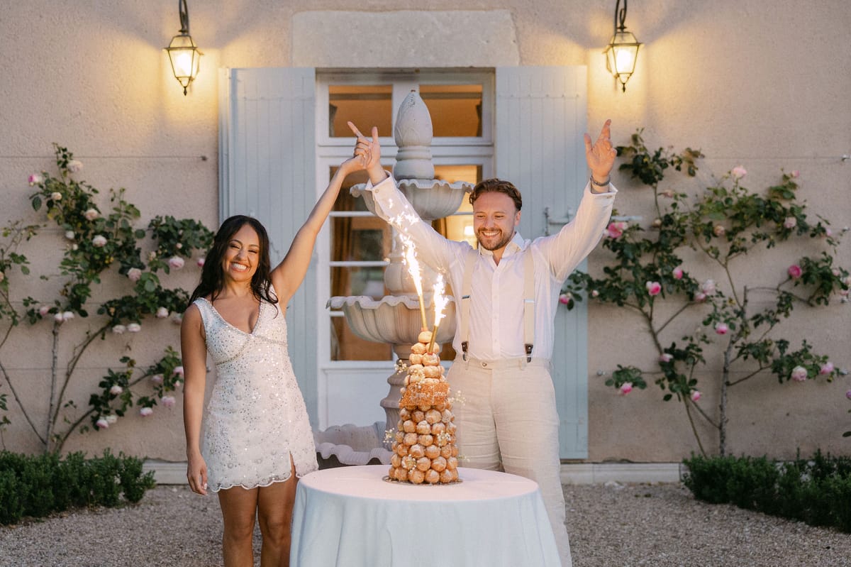 Bride and groom celebrating beside their croquembouche cake